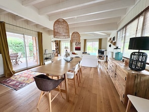 A spacious living area with a large wooden table, a sofa, and a television. There is a balcony with outdoor furniture. - New Listing (La Teste-de-Buch)