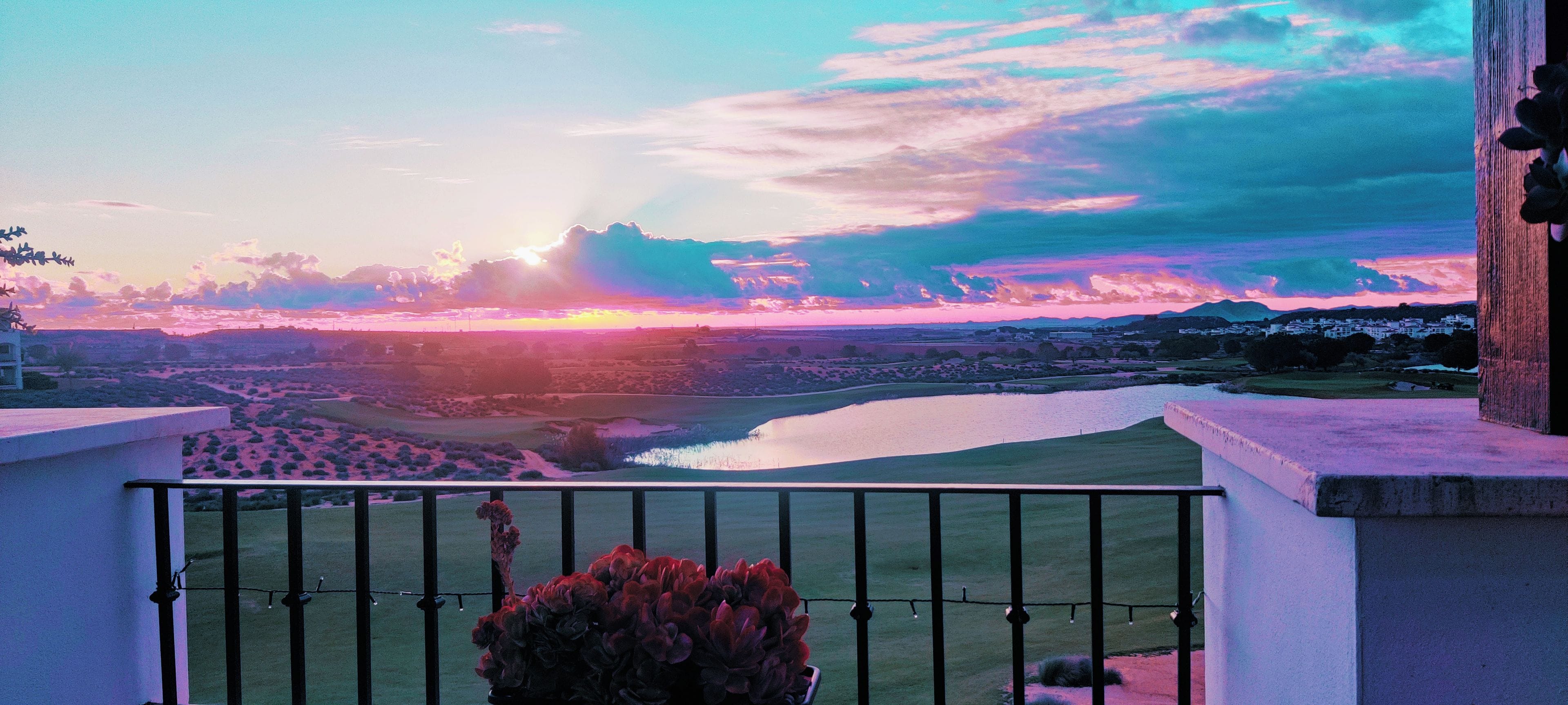 Un balcón con vistas a un atardecer sobre un paisaje con agua y edificios.