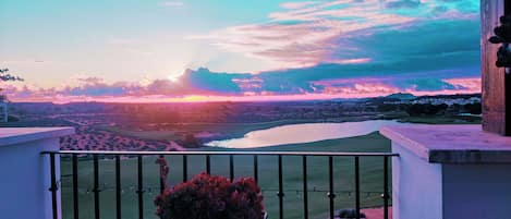 A balcony with a view of a sunset over a landscape with water and buildings.