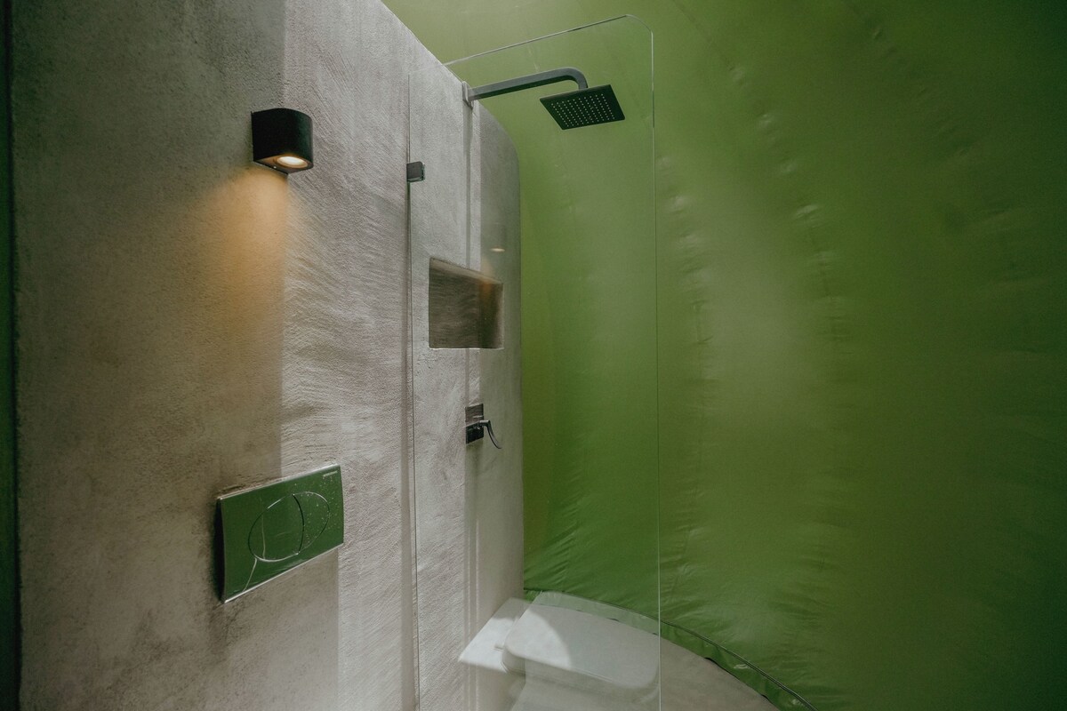 Une douche moderne dotée d’une paroi en verre, d’un luminaire fixé au mur et d’un pommeau de douche à main.