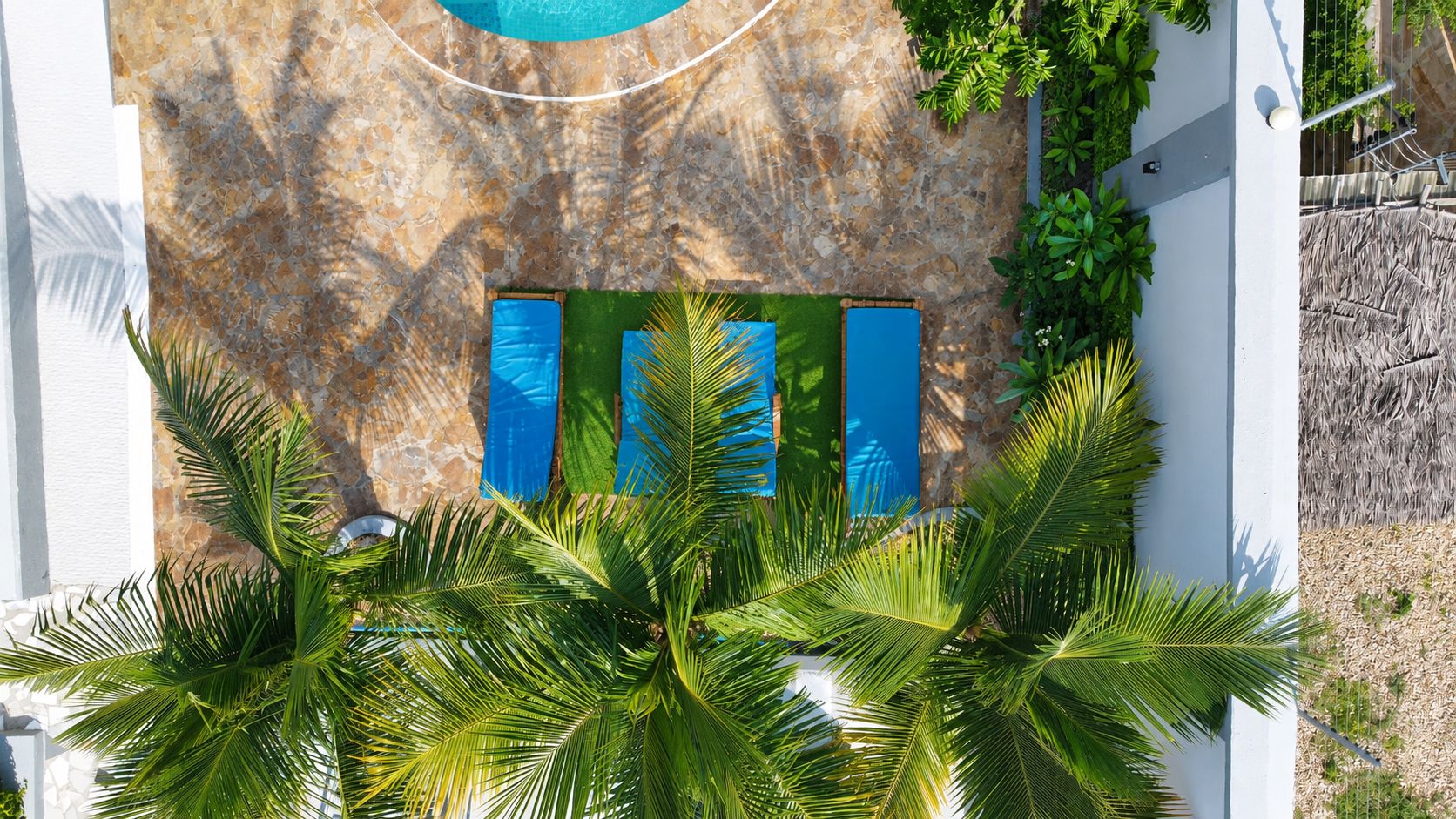 Una piscina con uno sfondo a muro in pietra, una porta blu e una rigogliosa vegetazione sul davanti.