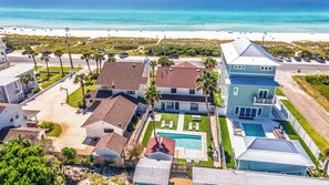 Un quartier résidentiel avec une grande maison dotée d’une piscine, d’un court de tennis et offrant une vue sur la plage.