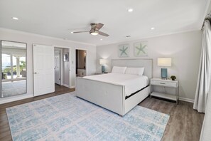Une chambre à coucher avec un lit, des tables de chevet, un ventilateur de plafond et des œuvres d’art accrochées au mur.