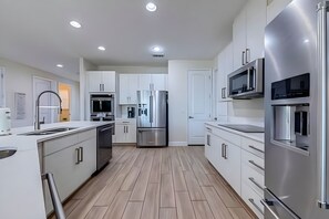 A modern kitchen with white cabinetry, stainless steel appliances, and a wooden floor. - ECR7654 - Family Oasis Retreat + Spa + Theater! (Kissimmee)