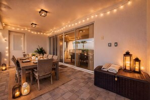 Ein Essbereich im Freien mit einem Tisch für vier Personen, umgeben von Korbstühlen, und einer Glasschiebetür, die auf eine Terrasse führt.