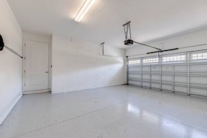 A clean, empty garage with a white door, a metal garage door, and a ceiling light fixture. - ECR7391 - Family Luxury Retreat + Pool @Encore! (Kissimmee)