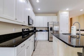 A modern kitchen with white cabinets, a black countertop, and stainless steel appliances. - ECR641 - Stunning Dream Vacation+Theater @Encore (Kissimmee)