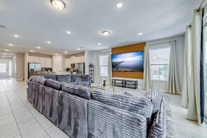 A modern living room with a large sectional sofa, a flat-screen TV, and a dining area with a table and chairs. - ECR313 - Resort Style Mansion + Gyn/Spa/Theater! (Kissimmee)