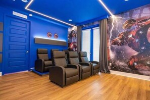 A room with a blue wall, a door, and a large poster of a space scene. There are three black chairs and a small table. - ECR7650 - Magic Villa | Theater | Game Room@Encore (Kissimmee)