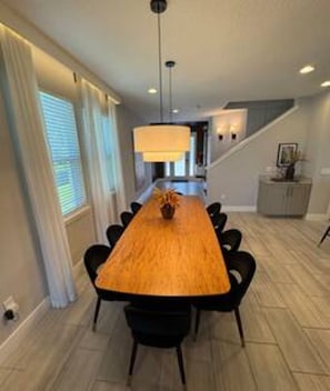 A dining area with a long wooden table, black chairs, and a hanging light fixture. - ECR7650 - Magic Villa | Theater | Game Room@Encore (Kissimmee)