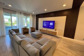 A modern living room with a large flat-screen TV, a sofa set, and a small table. - ECR7650 - Magic Villa | Theater | Game Room@Encore (Kissimmee)