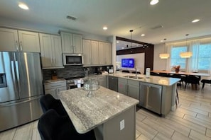 A modern kitchen with stainless steel appliances, a central island, and a dining area with a view. - ECR7650 - Magic Villa | Theater | Game Room@Encore (Kissimmee)