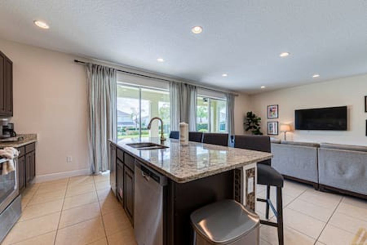 A modern kitchen with a central island, a dining area with a table and chairs, and a large window providing natural light.