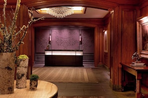 A lobby with a reception desk, a chandelier, wooden paneling, and a patterned wall. - St Regis Aspen Residence Club, Super Lux 2 Bedroom, 2.5 Bath Residence (Aspen)