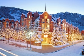 A large, multi-story hotel with a prominent central tower, surrounded by snow-covered trees and a mountainous backdrop. - St Regis Aspen Residence Club, Super Lux 2 Bedroom, 2.5 Bath Residence (Aspen)