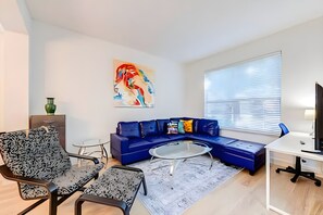 A modern living room with a sectional sofa, a glass coffee table, a patterned armchair, a small side table, and a large abstract painting on the wall. - EIR2706 - Lakefront Resort Home, 7B, 8 min to Disney (Kissimmee)