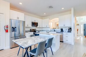 A modern kitchen with white cabinetry, stainless steel appliances, and a marble island with seating. - EIR2706 - Lakefront Resort Home, 7B, 8 min to Disney (Kissimmee)