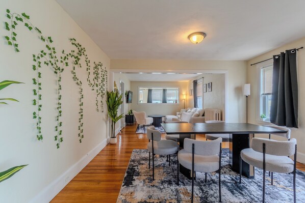 A modern living room with a dining area, wooden flooring, and a large window with curtains.