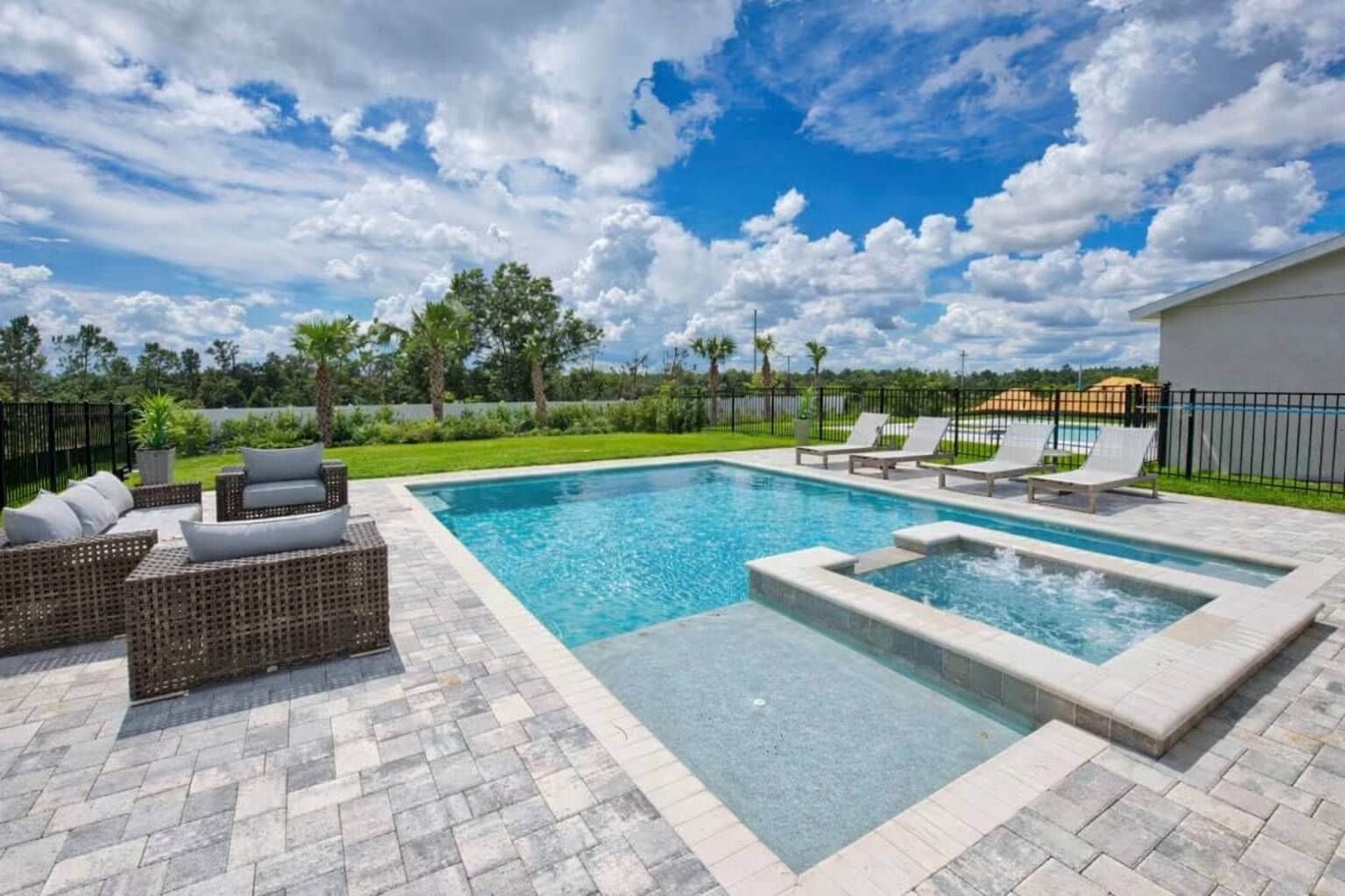 A swimming pool with lounge chairs and a hot tub area, surrounded by a paved deck.