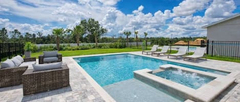A swimming pool with lounge chairs and a hot tub area, surrounded by a paved deck.