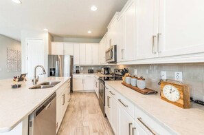 A modern kitchen with white cabinets, stainless steel appliances, and a wooden clock on the countertop. - ECR7676 - Bright Villa @Encore close from Disney! (Kissimmee)