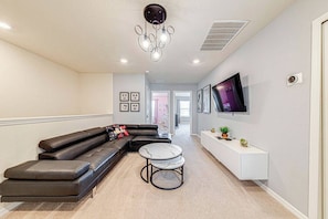 A modern living room with a sectional sofa, a round coffee table, a flat-screen TV mounted on the wall, and a white console table with decorative items. - WIR3753 - Family Resort Access Vacation @Disney (Davenport)