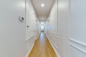 A long, narrow hallway with white walls and wooden flooring, leading to a room with a window and curtains. - ECR7609 - Enchanted Vacation Home @Encore (Kissimmee)
