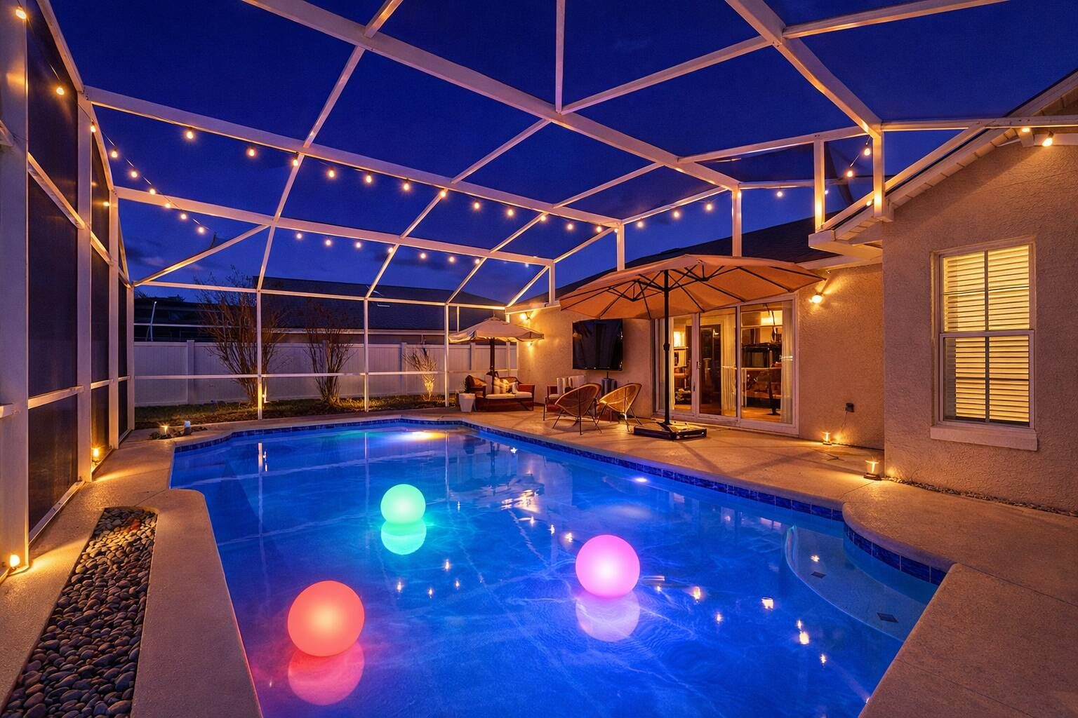 A swimming pool with a covered patio area, a television, and outdoor seating.