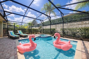 An outdoor swimming pool with two pink flamingo floats, lounge chairs, and a covered area with a view of palm trees. - ECR7407 - Disney Vacation Retreat @Encore (Kissimmee)