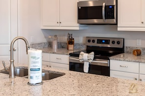 A kitchen with white cabinets, a stainless steel microwave, a stove, and a sink with a modern faucet. - ECR7783 - 4B Family Friendly Vacation @Encore! (Kissimmee)