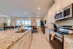 A modern kitchen with granite countertops, stainless steel appliances, and a dining area with a view. - ECR409 - Home 10 minutes from Disney @Encore (Kissimmee)