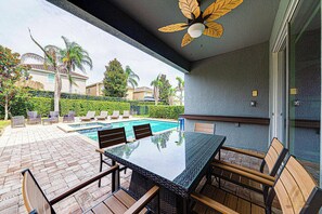 Une terrasse extérieure avec une table et des chaises à plateau en verre, une piscine et une vue sur un quartier résidentiel.