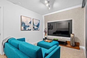 A modern living room with a large flat-screen TV, two abstract paintings, and a teal sofa. - ECR3385 Only 13 Minutes from Disney | Pool & GYN (Kissimmee)