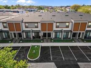 A modern multi-story building with a flat roof, multiple entry points, and a parking lot in front. - ECR3385 Only 13 Minutes from Disney | Pool & GYN (Kissimmee)