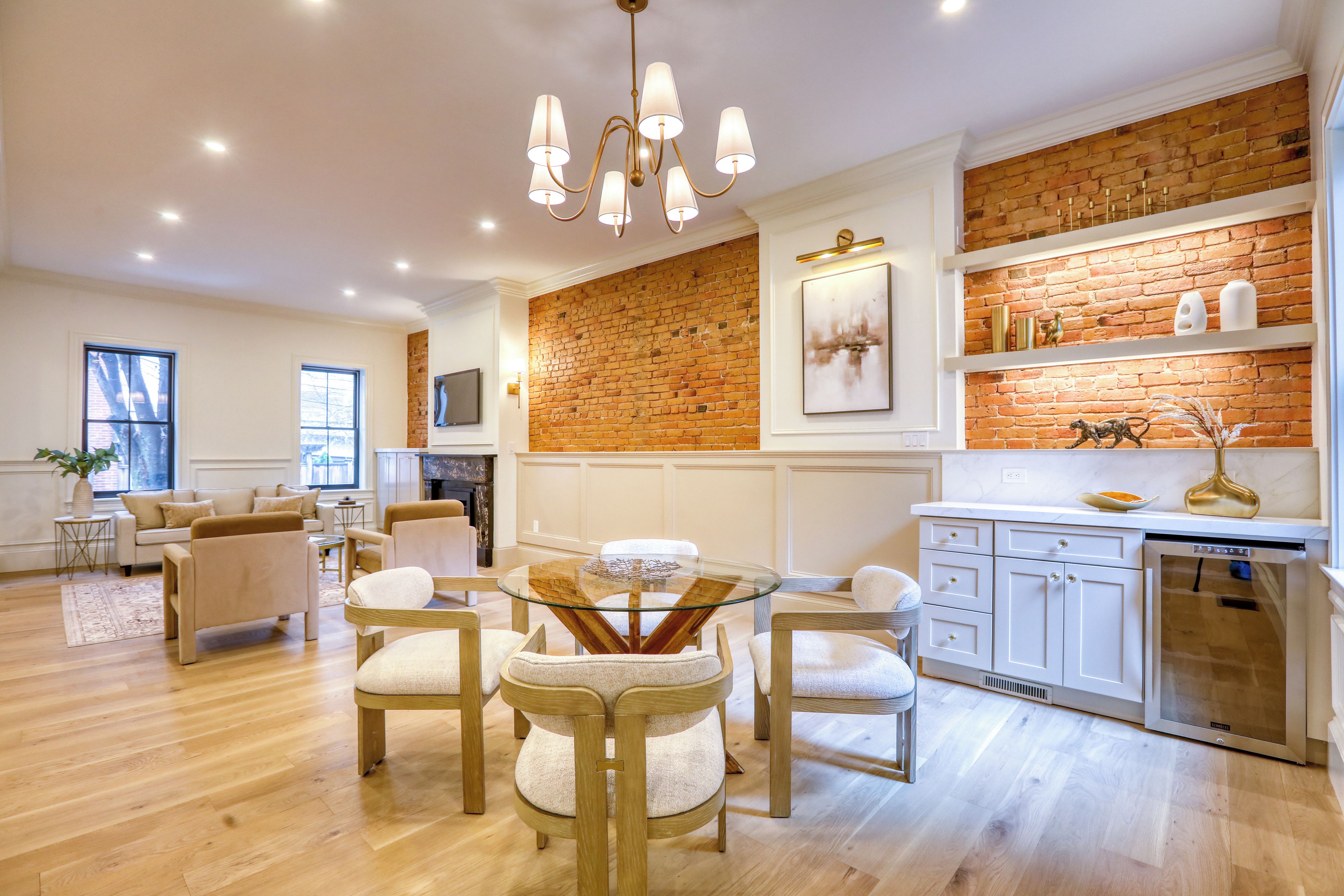 A modern kitchen with a brick accent wall, white cabinetry, and a dining area with a glass table and cushioned chairs.