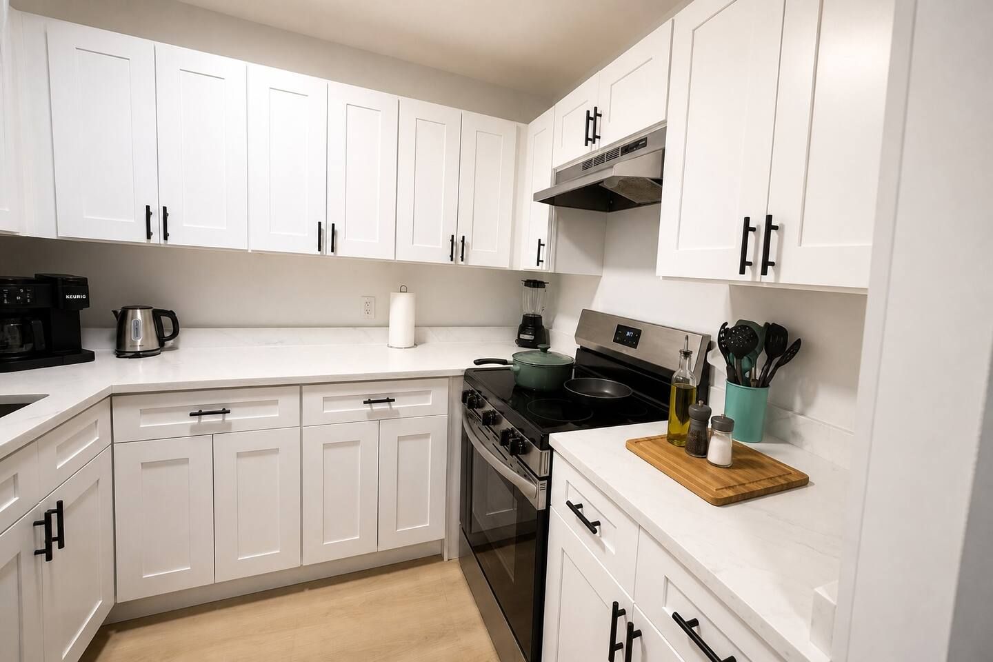 A modern kitchen with white cabinetry, a black stove, and a coffee maker.