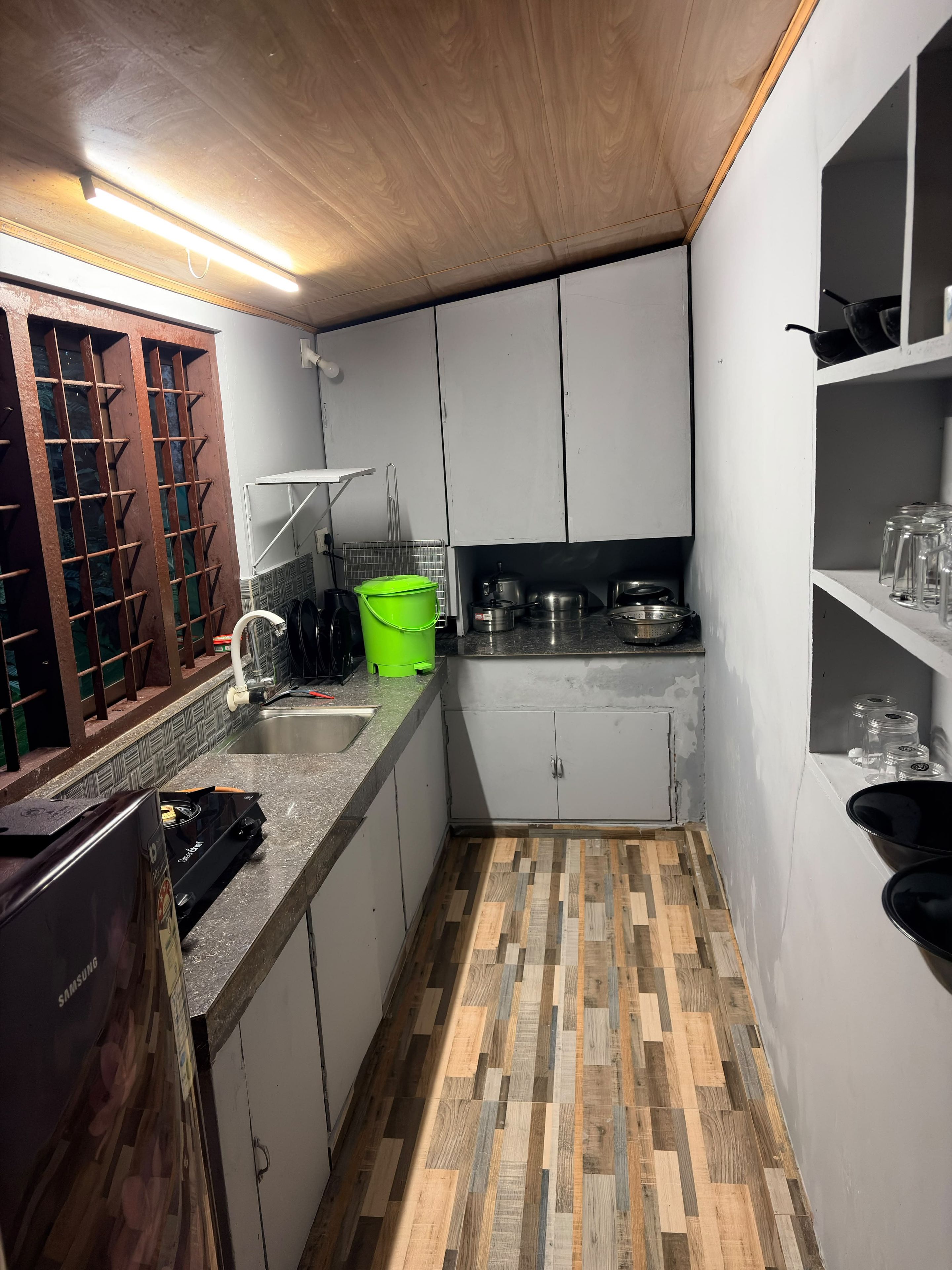 A compact kitchen with white cabinets, a wooden floor, and a countertop with various kitchen items.