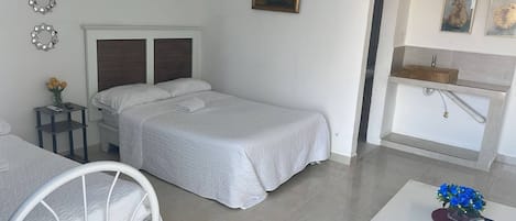 A bedroom with a bed, bedside table, and a small table with a vase of flowers.