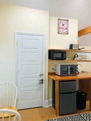 A compact kitchen with a white door, a microwave, a toaster, and a refrigerator. - Hollytree Cottage at Saluda River Farms (Greenville)