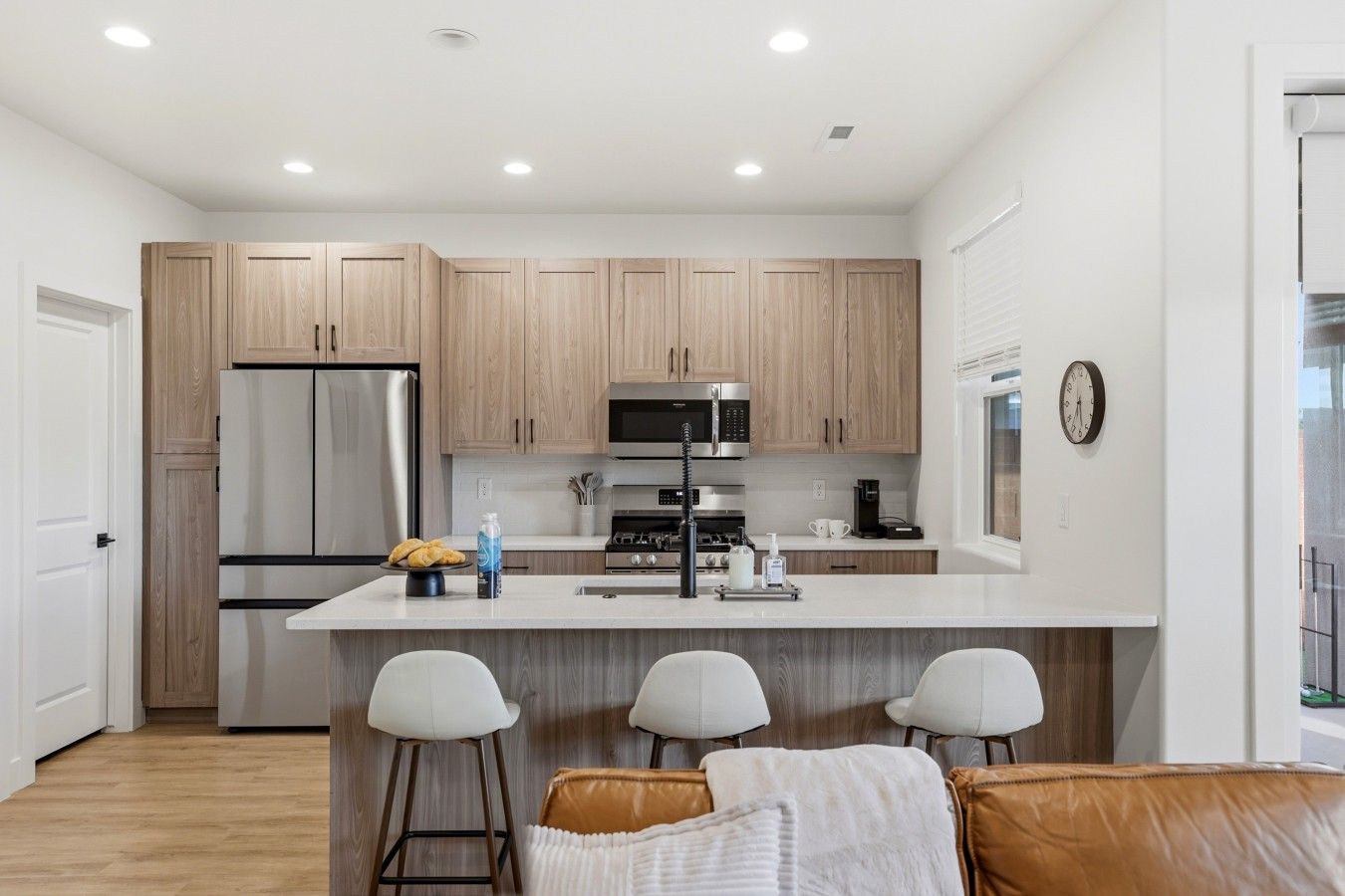 A modern kitchen with wooden cabinets, a stainless steel refrigerator, a microwave, and a central island with bar stools.