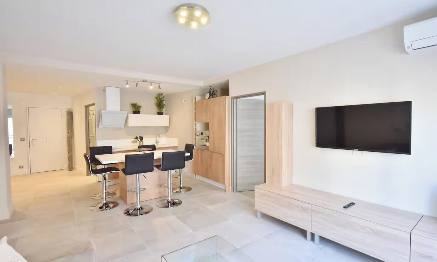 A modern kitchen with a dining area, a flat-screen TV mounted on the wall, and a sliding door closet.