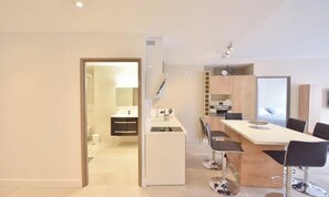 A modern kitchen with a central island, a dining area with a long table and chairs, and a visible bathroom with a mirror and sink. - IDEALLY LOCATED JUST A TWO-MINUTE WALK FROM THE ICONIC CROISETTE (Cannes)