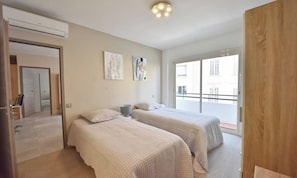 Ein Schlafzimmer mit zwei Betten, einem Fenster und einer Tür zu einem anderen Raum.