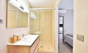Ein modernes Badezimmer mit einer gläsernen Dusche, einem weißen Waschbecken mit Holzunterschrank und einem großen Spiegel.