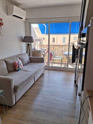 A living room with a sofa, a lamp, and a view of the outside balcony. - New Listing (Le Grau-du-Roi)