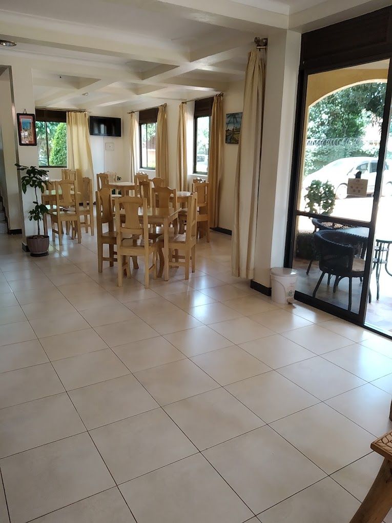 A spacious dining area with multiple wooden tables and chairs, a television mounted on the wall, and large windows with curtains.