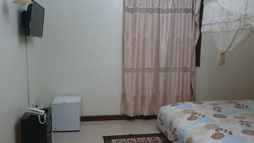 A bedroom with a bed, a television mounted on the wall, a small white appliance, and a curtain.