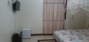 A bedroom with a bed, a television mounted on the wall, a small white appliance, and a curtain. - The Dove's Nest Hotel Gulu (Gulu)
