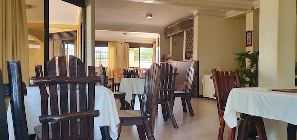 Un espace repas avec des chaises et des tables en bois, un coin cuisine et une plante en pot.