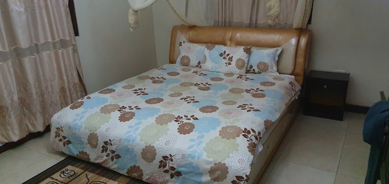 Een slaapkamer met een bed, gordijnen, een hoofdeinde, een nachtkastje en een vloerkleed.